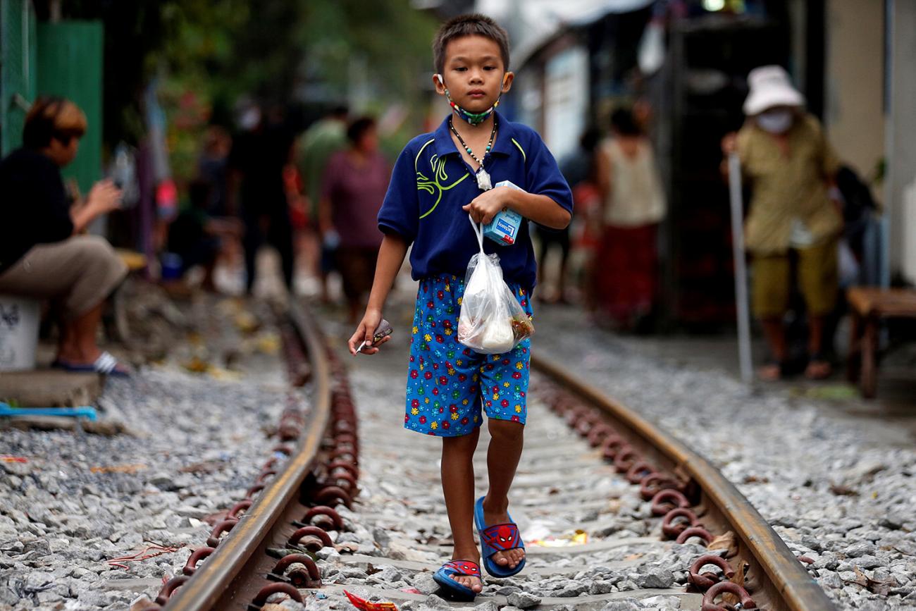 The photo shows a boy carrying a plastic bag walking toward the camera along train tracks.