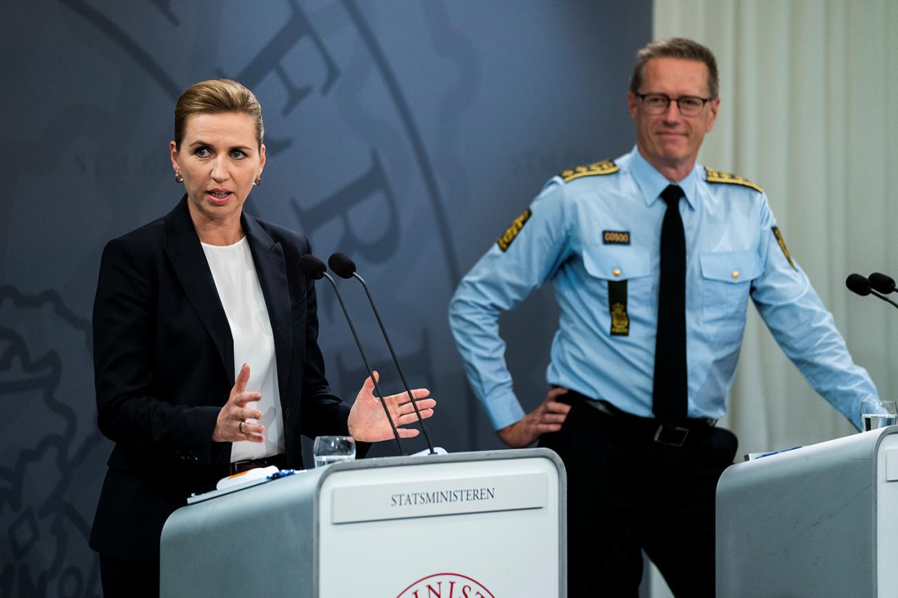 The photo shows the PM speaking at a podium while the police chief in the background looks on.