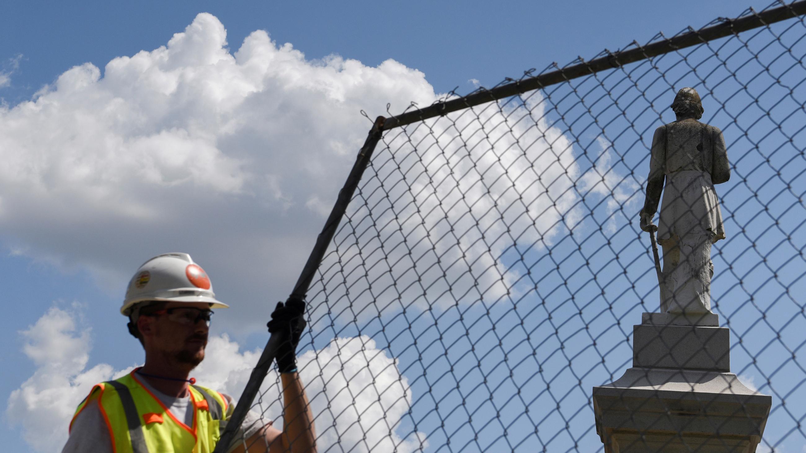 The photo shows a worker holding a piece of fencing. The controversial statue can be seen in the background.