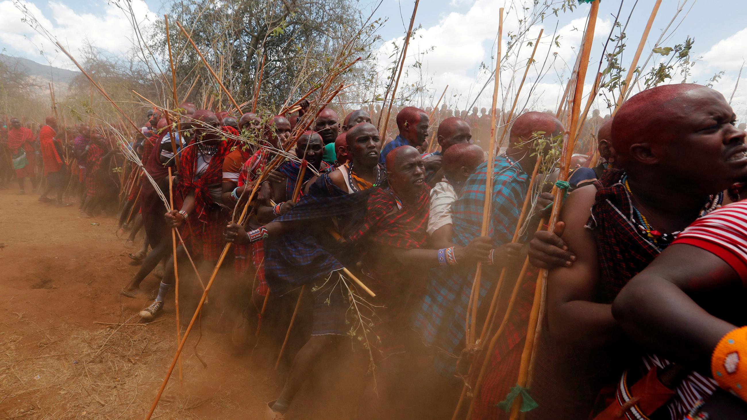 The photo shows a rite of passage ceremony with a crowd of young and old men holding sticks and kicking up a lot of dust.